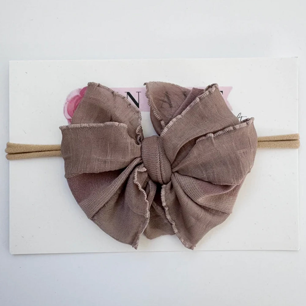A large fabric bow headband in a dusty taupe-brown color, displayed on a white backing card.
