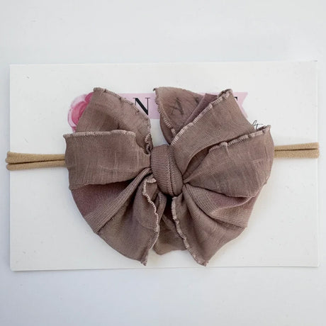 A large fabric bow headband in a dusty taupe-brown color, displayed on a white backing card.
