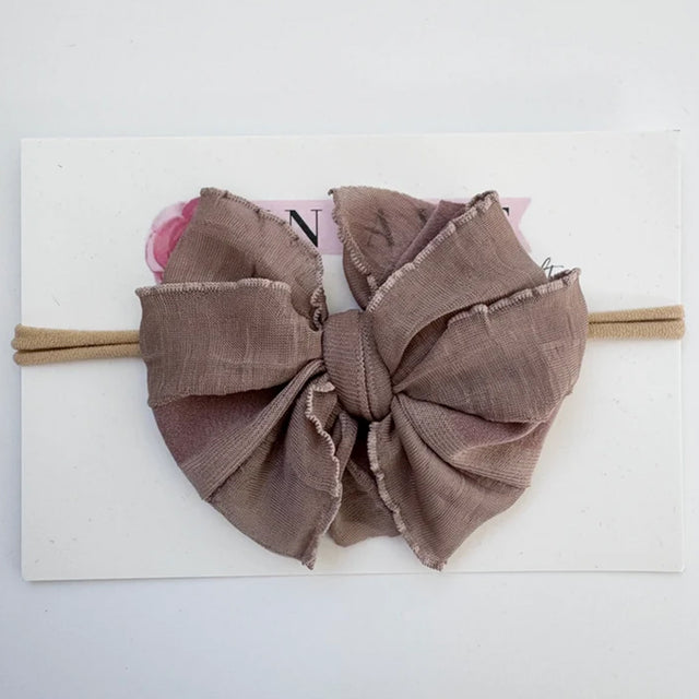 A large fabric bow headband in a dusty taupe-brown color, displayed on a white backing card.