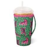 A green neoprene travel tumbler sleeve with a pink leopard print and pink tiger illustrations, shown on a clear-lidded insulated cup with a straw against a white background.