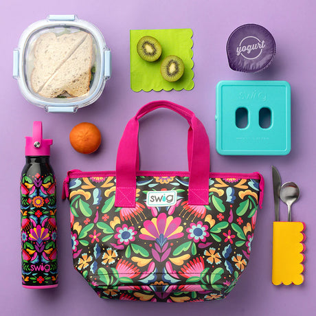 A flat-lay of Swig branded lunch accessories on a lavender background, including a floral insulated tote bag, patterned water bottle, lunchbox, yogurt container, utensils, and fruit.