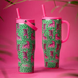 Two pink and green insulated tumblers with seahorse prints, shown on a bright pink background with decorative palm leaves.
