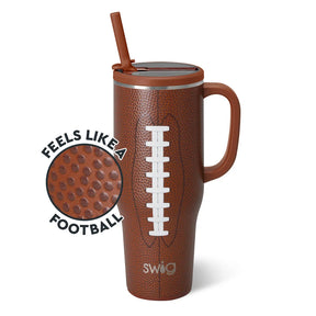 A brown football-texture handled tumbler with a lid and straw, shown on a white background with a circular inset highlighting the textured surface and the words 'FEELS LIKE A FOOTBALL'. The tumbler has a white laces graphic and the Swig logo near the bottom.