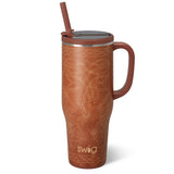 A brown insulated travel tumbler with a handle, a matching brown lid and straw, and a light beige stitched floral pattern on the front. The brand name 'swig' is printed near the bottom.