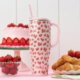 Pink swig tumbler with strawberry pattern surrounded by strawberries, cake, and pastries on a white background