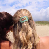 Two women on a beach with one wearing a hair clip.