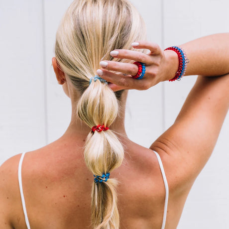 Woman with blonde hair tied in a ponytail using colorful hair ties against a light background