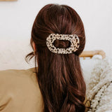 Person with long brown hair wearing a leopard print hair clip, sitting on a couch.