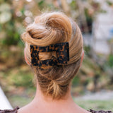 Person with blonde hair styled in an updo with a leopard print hair clip, outdoors.