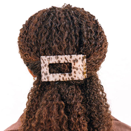 Person with curly hair wearing a leopard print hair clip on a white background