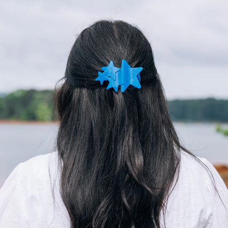 Person with blue hair clip shaped like stars against a natural background
