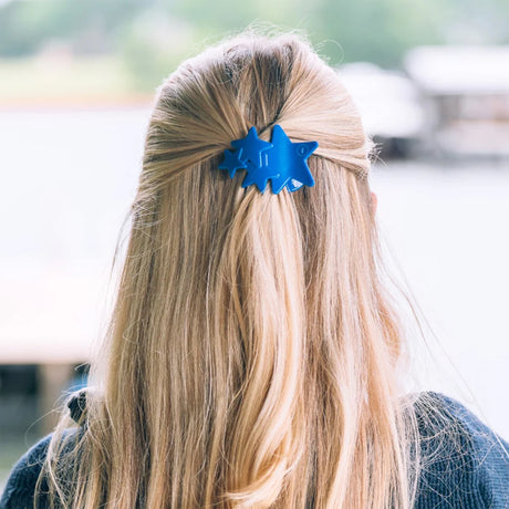 Person with blue hair clip in blonde hair, blurred outdoor background
