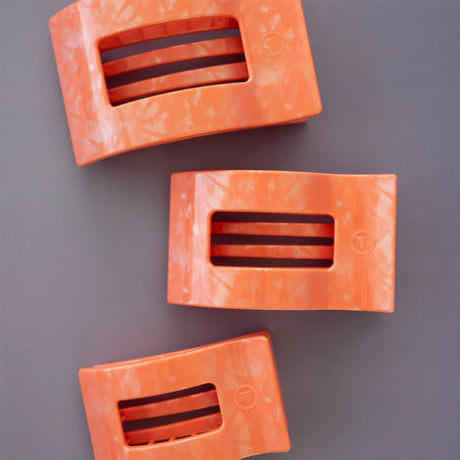 Three orange plastic clips with black straps on a gray background