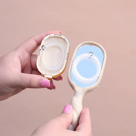 Hand holding a compact mirror with a brush on a beige background