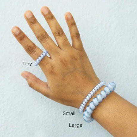 Hand wearing a bracelet with labeled sizes 'Tiny', 'Small', and 'Large' on a white background.