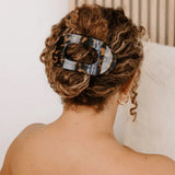 Person with styled hair featuring a tortoiseshell hair clip against a neutral background