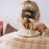 Person with a bun holding a checkered blanket, wearing a patterned hair clip.