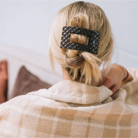 Person with a bun holding a checkered blanket, wearing a patterned hair clip.