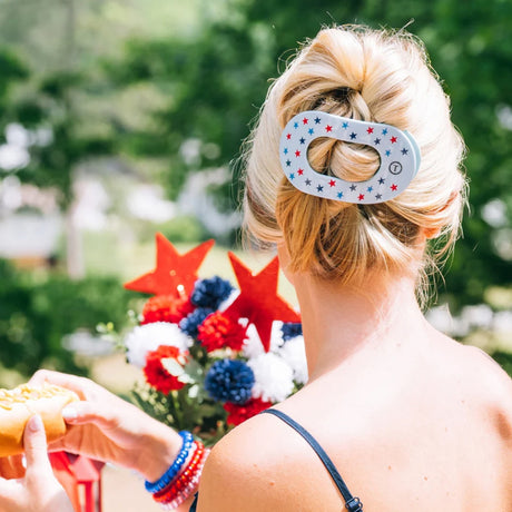 Person with a patriotic hair clip holding a hot dog outdoors
