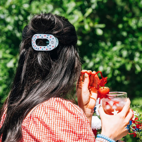 Person with a hair clip holding a drink outdoors