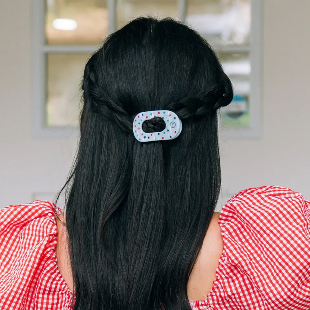 Person with long black hair wearing a decorative hair clip, wearing a red and white checkered shirt.
