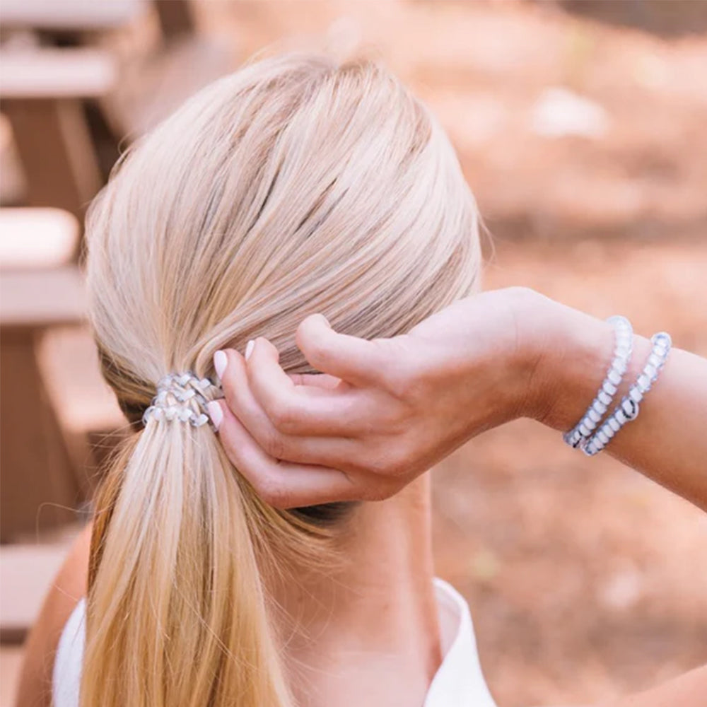 Person styling their blonde hair with a hair tie, wearing a bracelet.