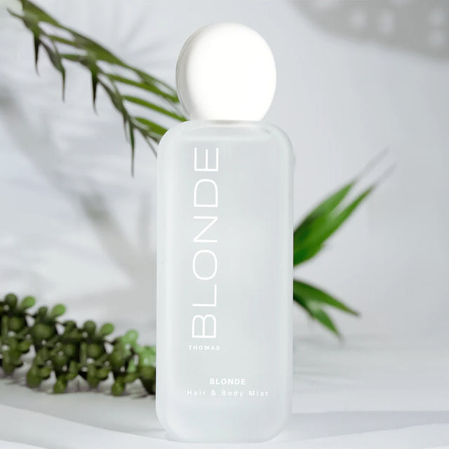 Bottle of 'Blonde' hair and body mist with green leaves in the background