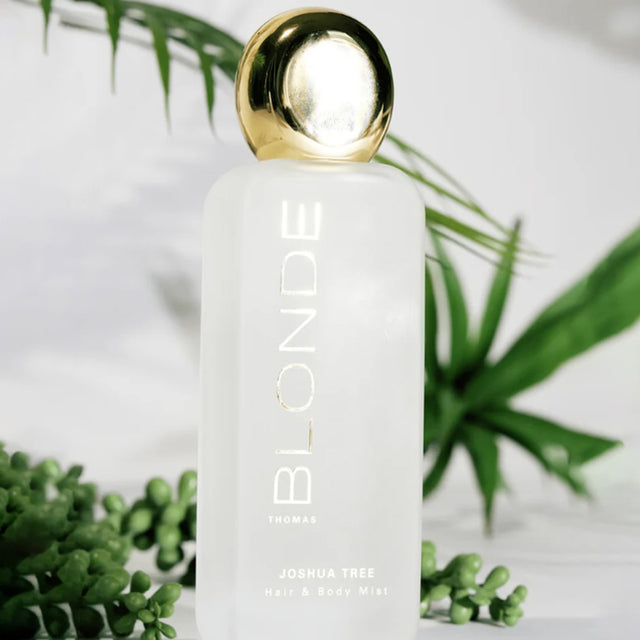 White bottle with gold cap labeled 'BLOUNDE' surrounded by green plants on a light background