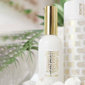 White skincare bottle with gold cap and branding against a blurred natural background