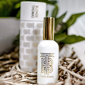 White and gold bottle with 'THOMAS BLONDE' branding on a natural background