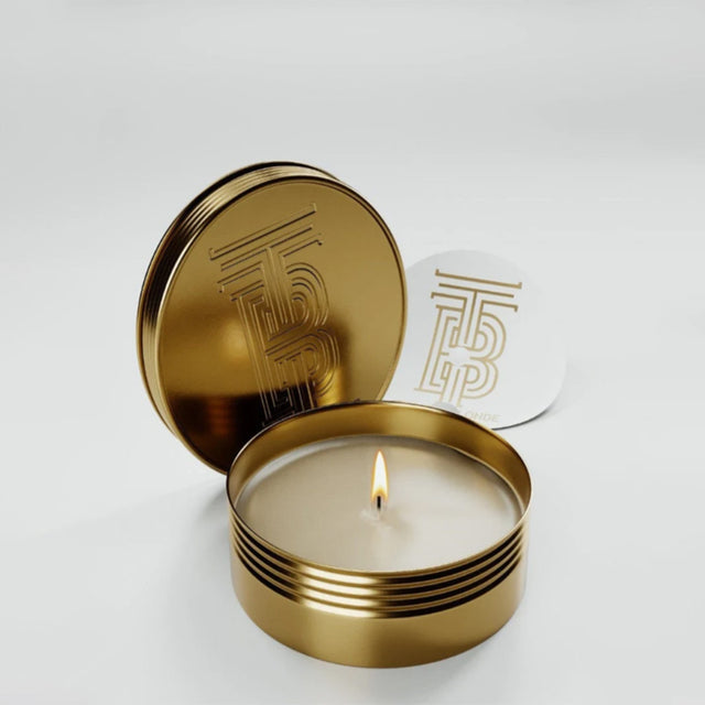 Gold candle tin with a lit candle inside on a white background