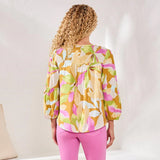 Woman wearing a colorful floral blouse and pink pants against a white background