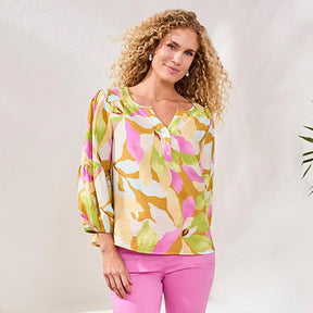 Woman wearing a colorful floral blouse and pink pants against a white background