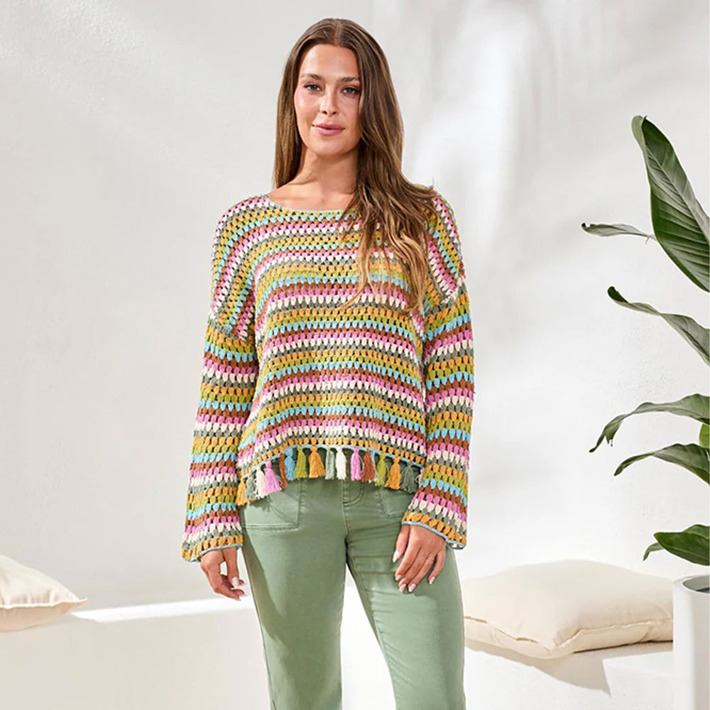 Woman wearing a colorful striped sweater in a bright room with a plant.