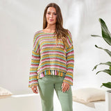 Woman wearing a colorful striped sweater in a bright room with a plant.