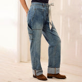 A person wearing light blue wide-leg denim jeans with cargo pockets and a striped tie belt, paired with brown suede boots, shown from the waist down in a bright indoor setting.
