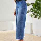 Person wearing blue jeans standing in a room with a plant in the background
