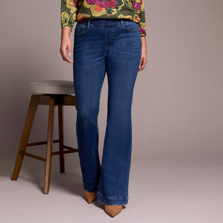 Person wearing blue jeans with a floral top and wooden stool in the background