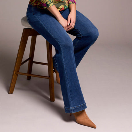 Person wearing blue jeans sitting on a wooden stool against a plain background