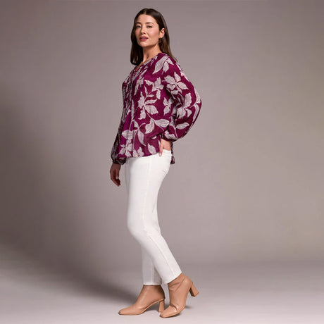 Woman wearing a purple floral blouse and white pants against a gray background