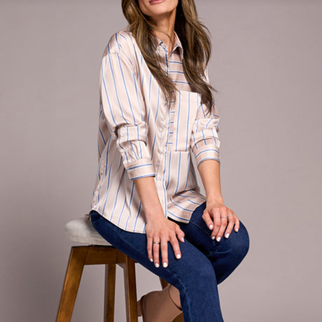 Woman wearing a striped shirt and jeans sitting on a stool against a gray background