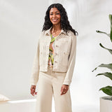 Woman wearing a beige denim jacket and pants in a minimal indoor setting