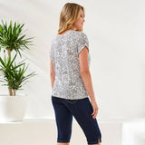 Woman wearing a patterned shirt and dark jeans standing in a room with plants.