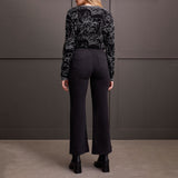 Person wearing a black patterned sweater and black pants against a gray wall.