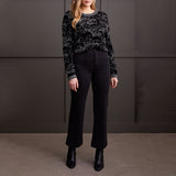 Woman wearing a black patterned sweater and black pants against a dark background