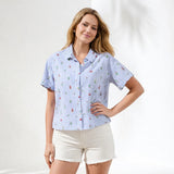Woman wearing a blue patterned shirt and white shorts on a plain background