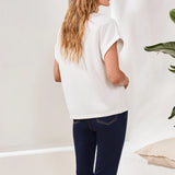 Person wearing a white sleeveless top and dark blue jeans against a plain background