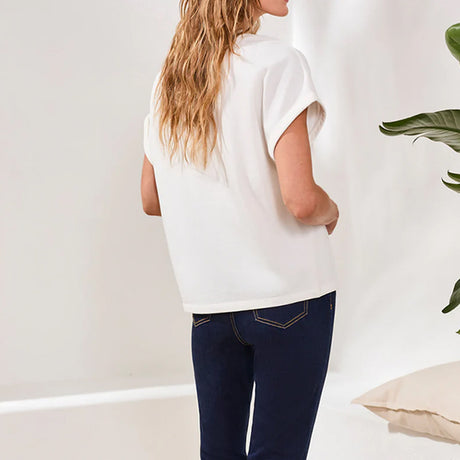 Person wearing a white sleeveless top and dark blue jeans against a plain background
