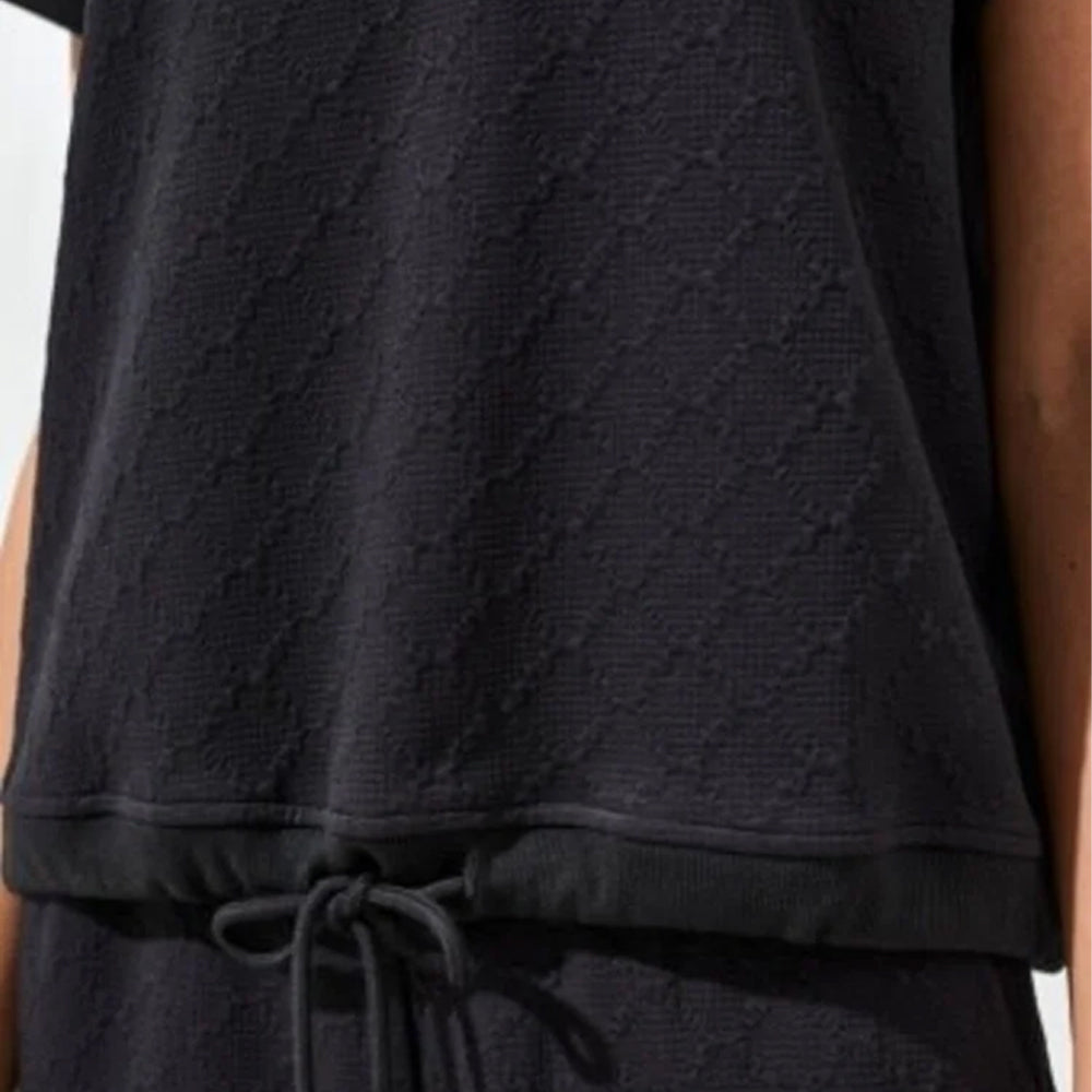 Black textured sleeveless top worn by a person on a light gray background