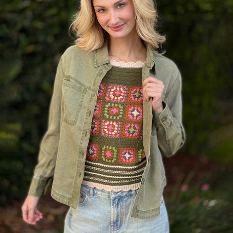 Woman wearing a green jacket over a colorful crochet sweater with a blurred natural background